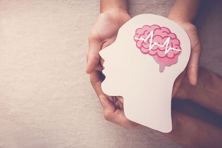Mãos segurando uma silhueta de cabeça com um cérebro ilustrado, representando a Terapia Cognitivo-Comportamental